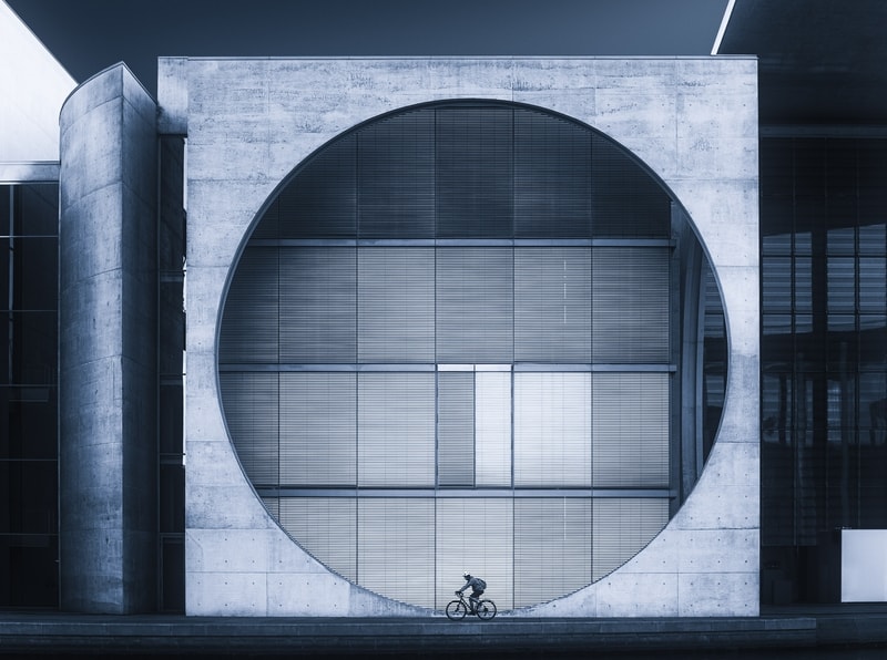 A cyclist on his bike in front of a building and a perfectly round vent.