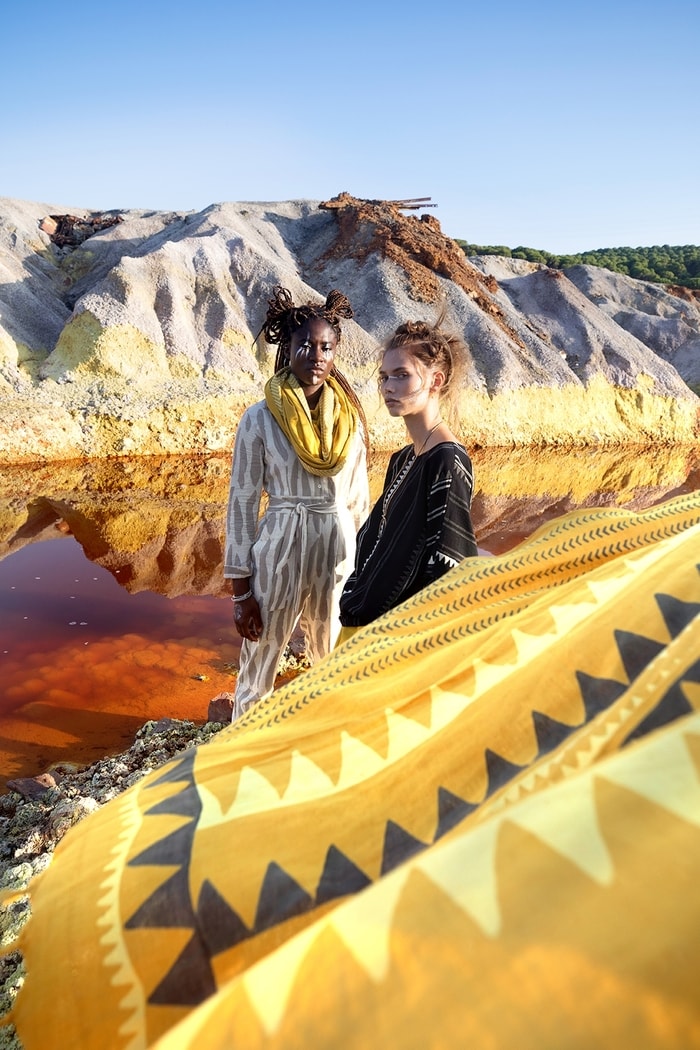 Two women in front of a red-coloured lake in tribal outfits