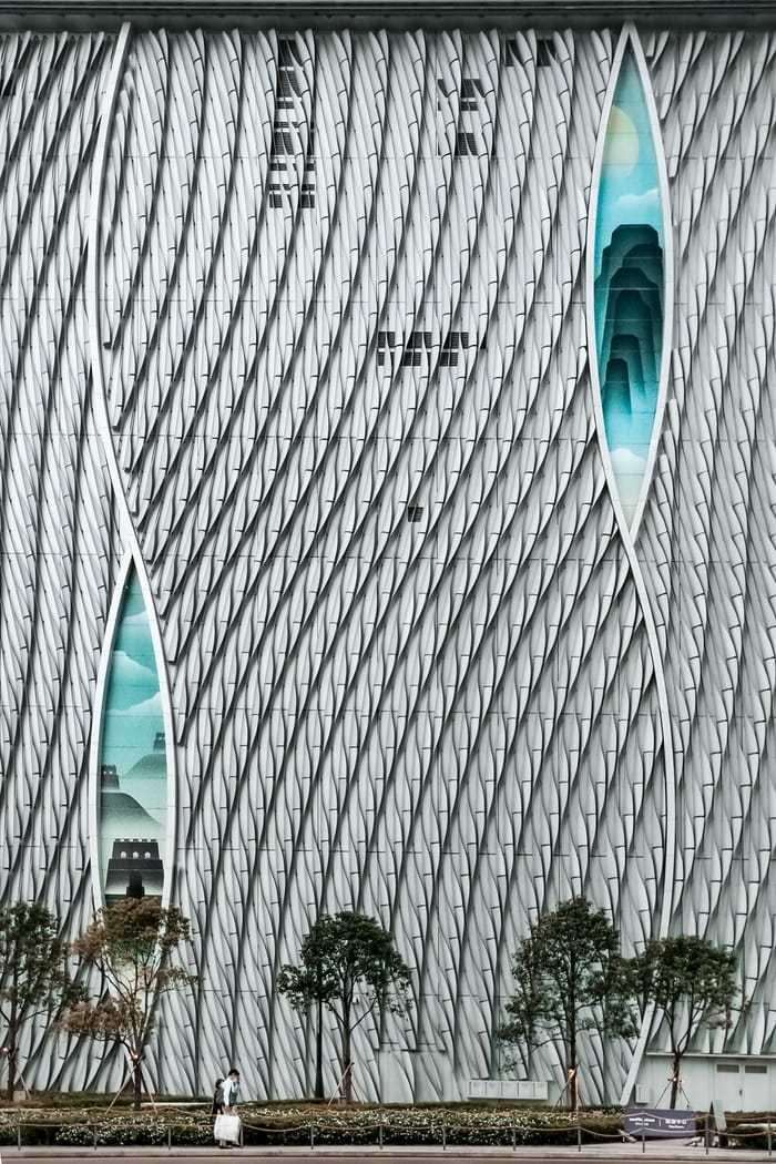 A Hong Kong building, large, with trees in the bottom, amazing geometrical shapes and blue slivers.